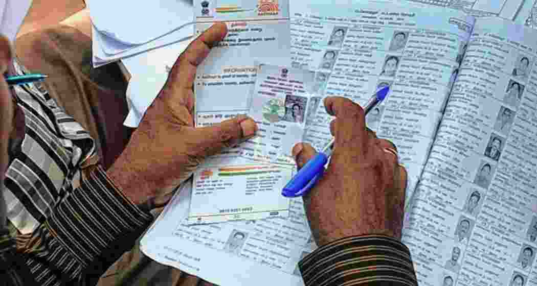 An election official checks an Aadhaar and voter card.