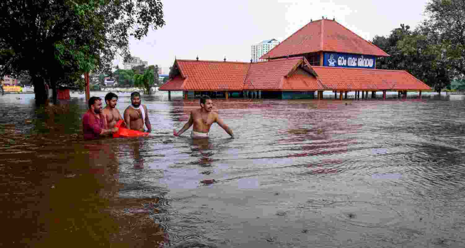 Kochi: People make their way through a flooded area near the Aluva Mahadeva Temple which got partially submerged due to rising water levels of the Periyar river following heavy rains, in Kochi district, Tuesday. Kochi: People make their way through a flooded area near the Aluva Mahadeva Temple which got partially submerged due to rising water levels of the Periyar river following heavy rains, in Kochi district, Tuesday.