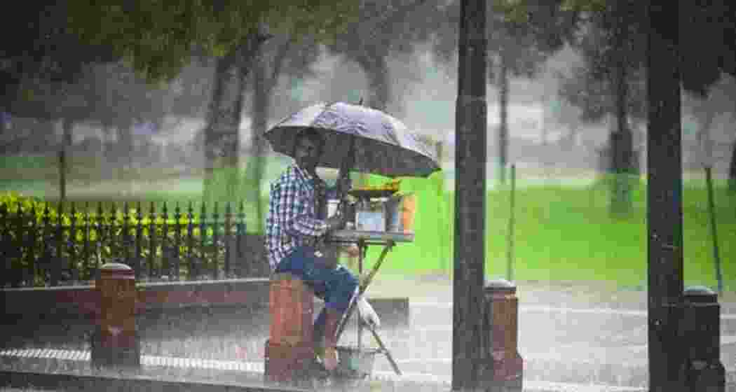 A snack vendor takes shelter beneath umbrellas as heavy rain lashes Kolkata.
