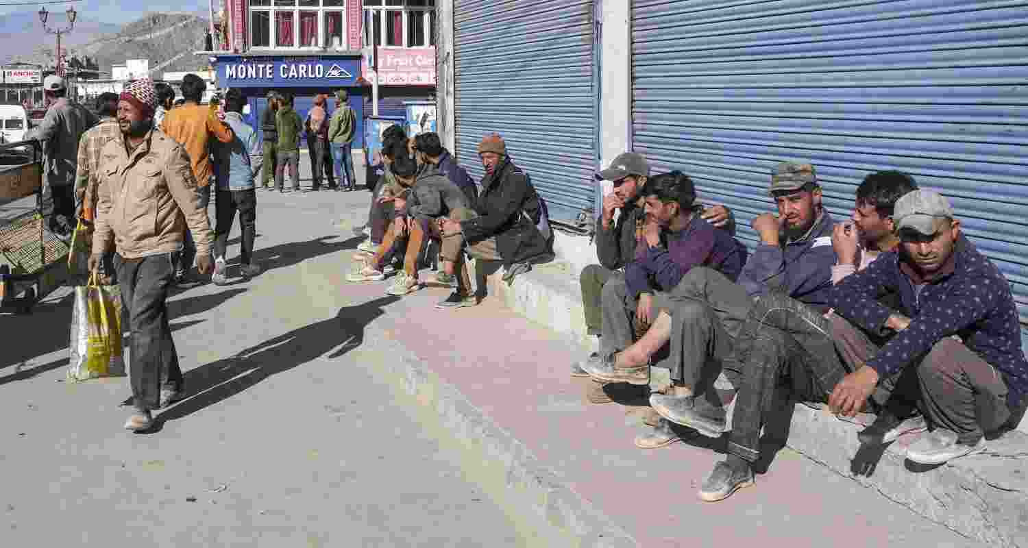 Workers wait outside a shop at a market during relaxation in curfew, in Leh, on Thursday.