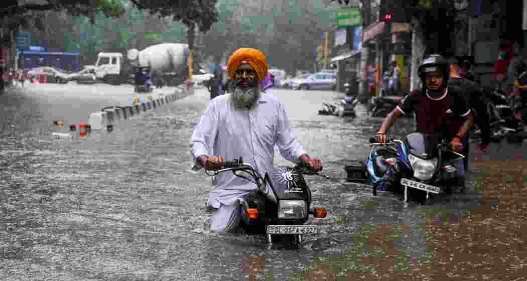 Motorcyclists stranded on a flooded street in Gurugram following torrential rainfall that submerged several parts of the NCR, triggering traffic chaos and an Orange Alert.