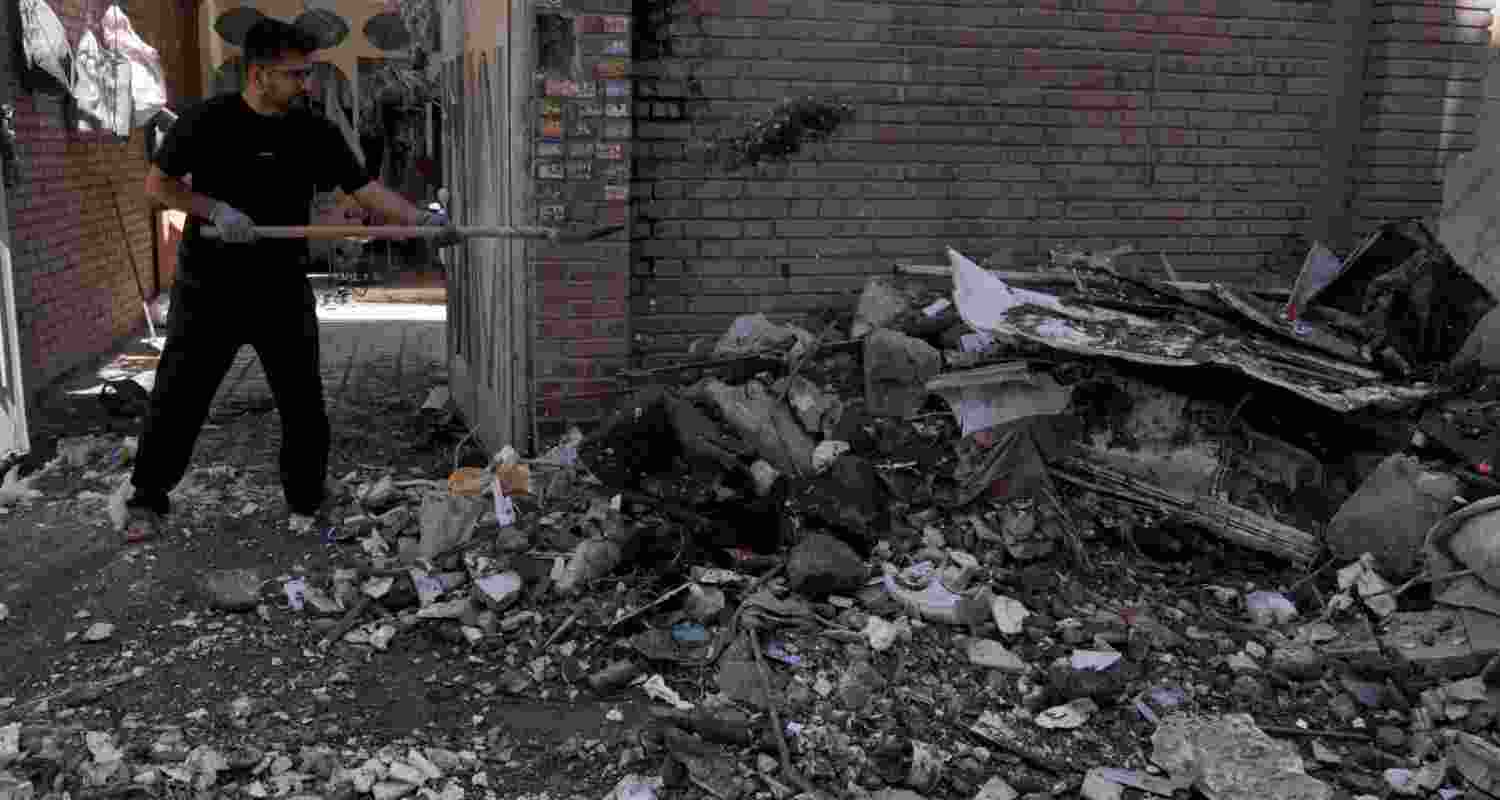 A man clears debris from a building damaged after a nearby residential building was hit in a US-Israeli strike in Tehran, Friday, March 27, 2026.