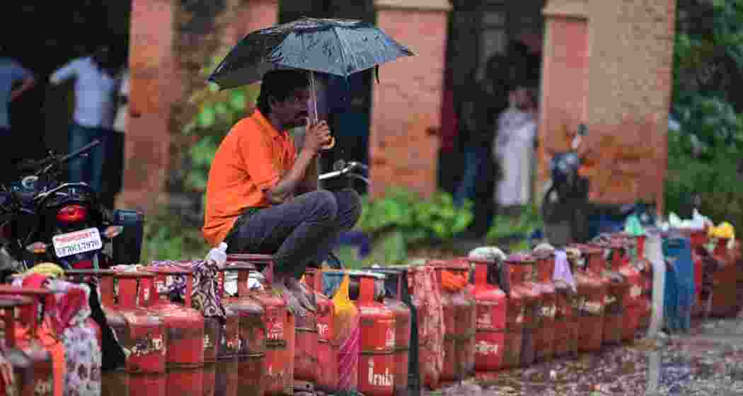 A man sits over an LPG cylinder amid rainfall, during an ongoing supply crisis, in Prayagraj, on Friday.