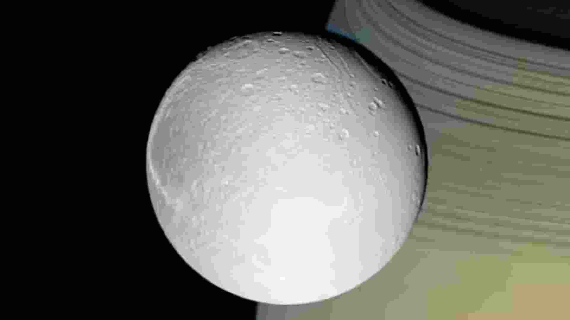 Dione, one of Saturn’s 274 moons, viewed with Saturn and its rings in the background.
