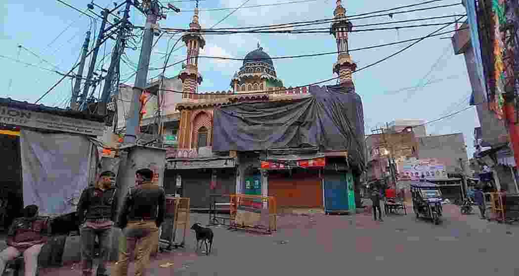 Security personnel stand guard along the Juta Maar Holi procession route in Shahjahanpur as a mosque could be seen covered with tarpaulin sheets ahead of the annual event.