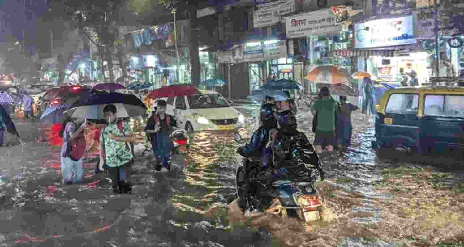 Commuters wade through a waterlogged road following rainfall, at Matunga, in Mumbai, Monday.