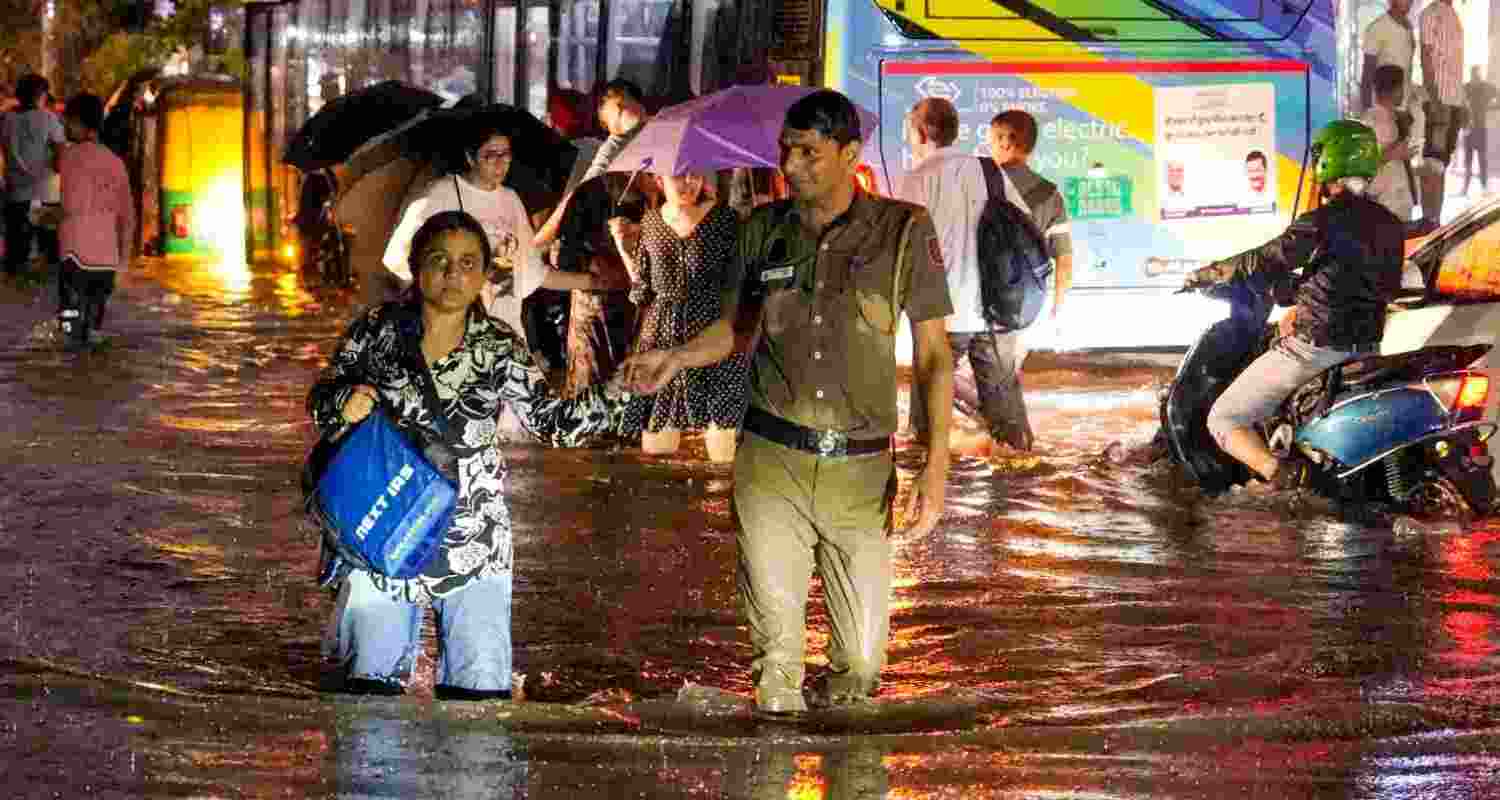 A woman being assisted by a police official while wading through a waterlogged road during rain near Pusa Road area, in New Delhi, Wednesday. A woman being assisted by a police official while wading through a waterlogged road during rain near Pusa Road area, in New Delhi, Wednesday.