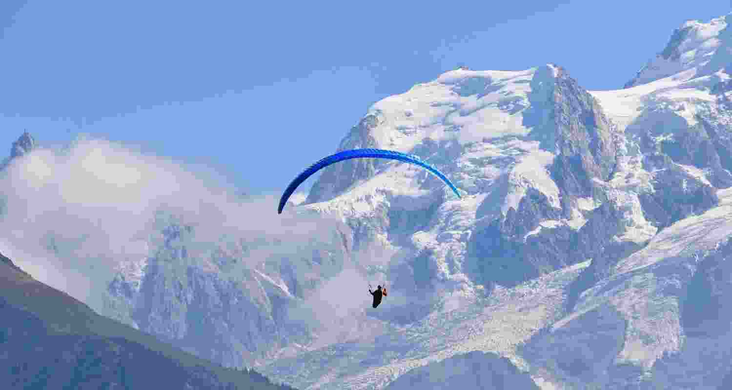 A paraglider in the air against snow capped mountains. A paraglider in the air against snow capped mountains.
