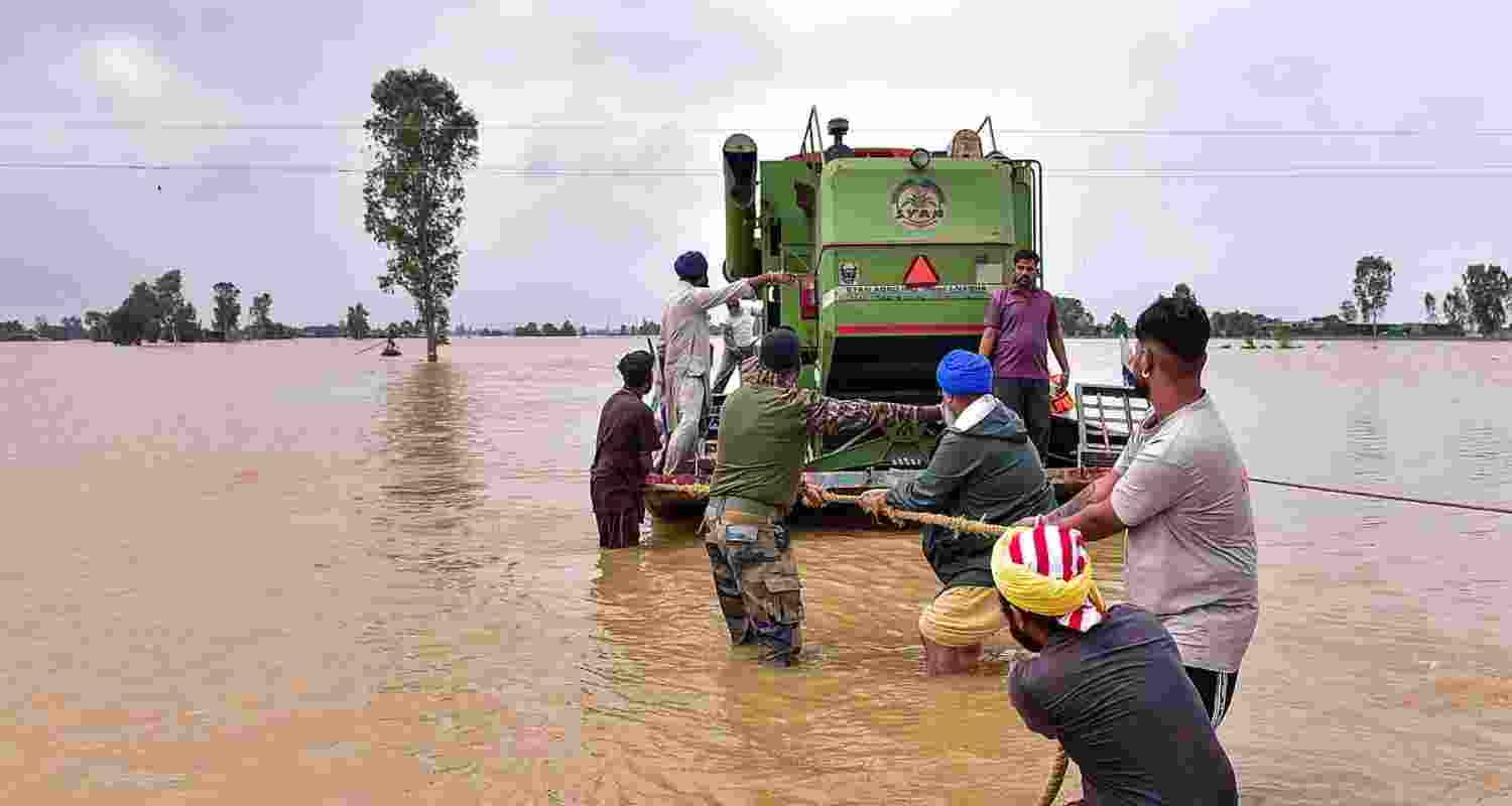 Security personnel and locals pull a boat loaded with an agricultural machine, through a flooded area, in Kapurthala, Punjab. Security personnel and locals pull a boat loaded with an agricultural machine, through a flooded area, in Kapurthala, Punjab.
