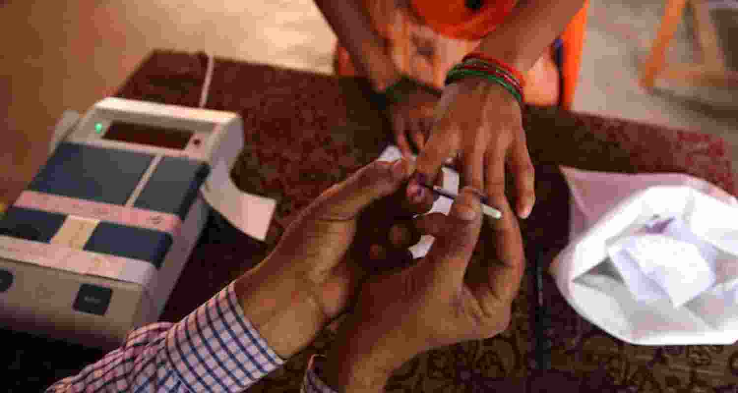 An election booth worker applies indelible to a voter's finger. An election booth worker applies indelible to a voter's finger.