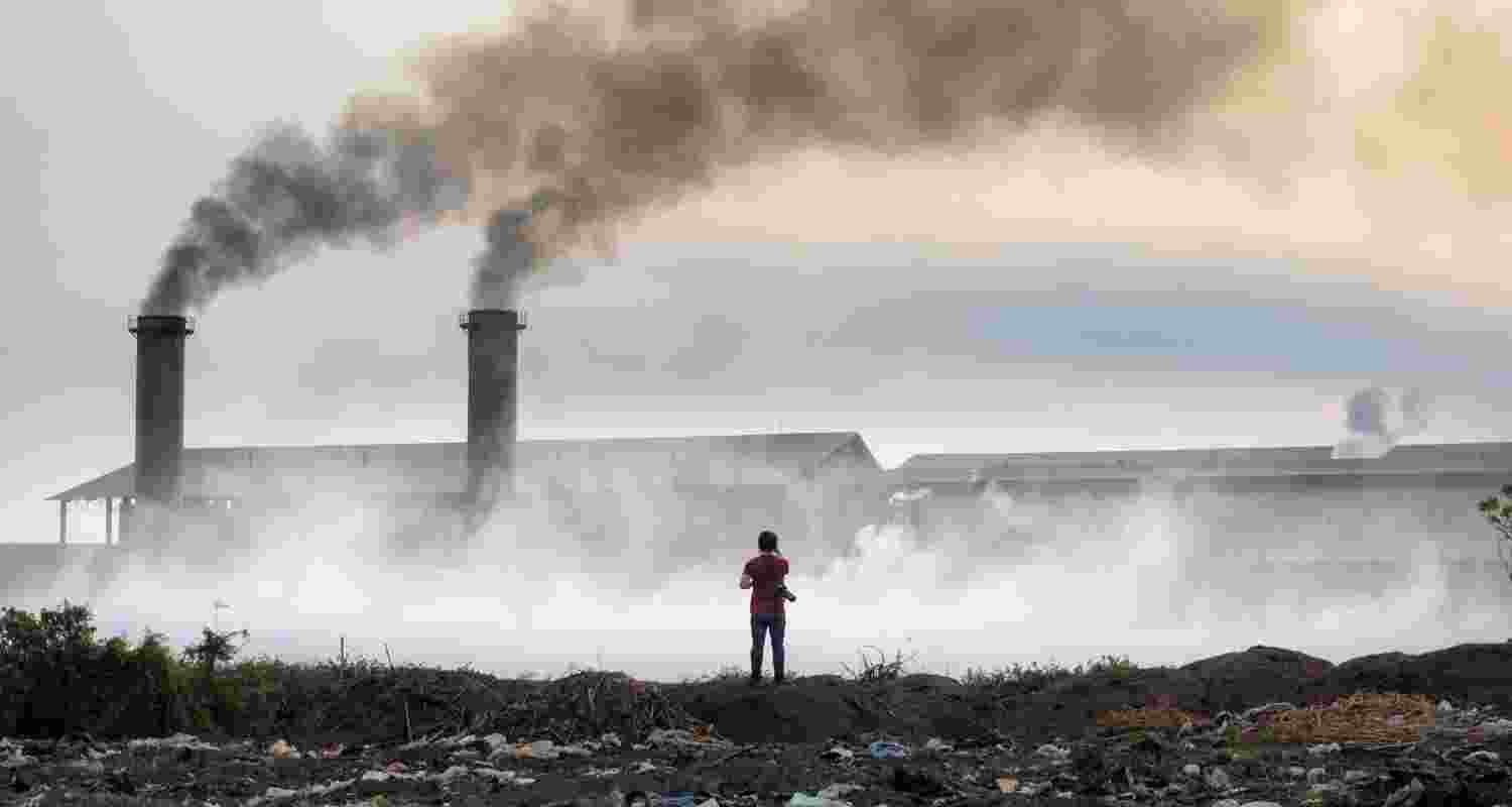 A man stands next to a factory releasing toxic gases. A man stands next to a factory releasing toxic gases.