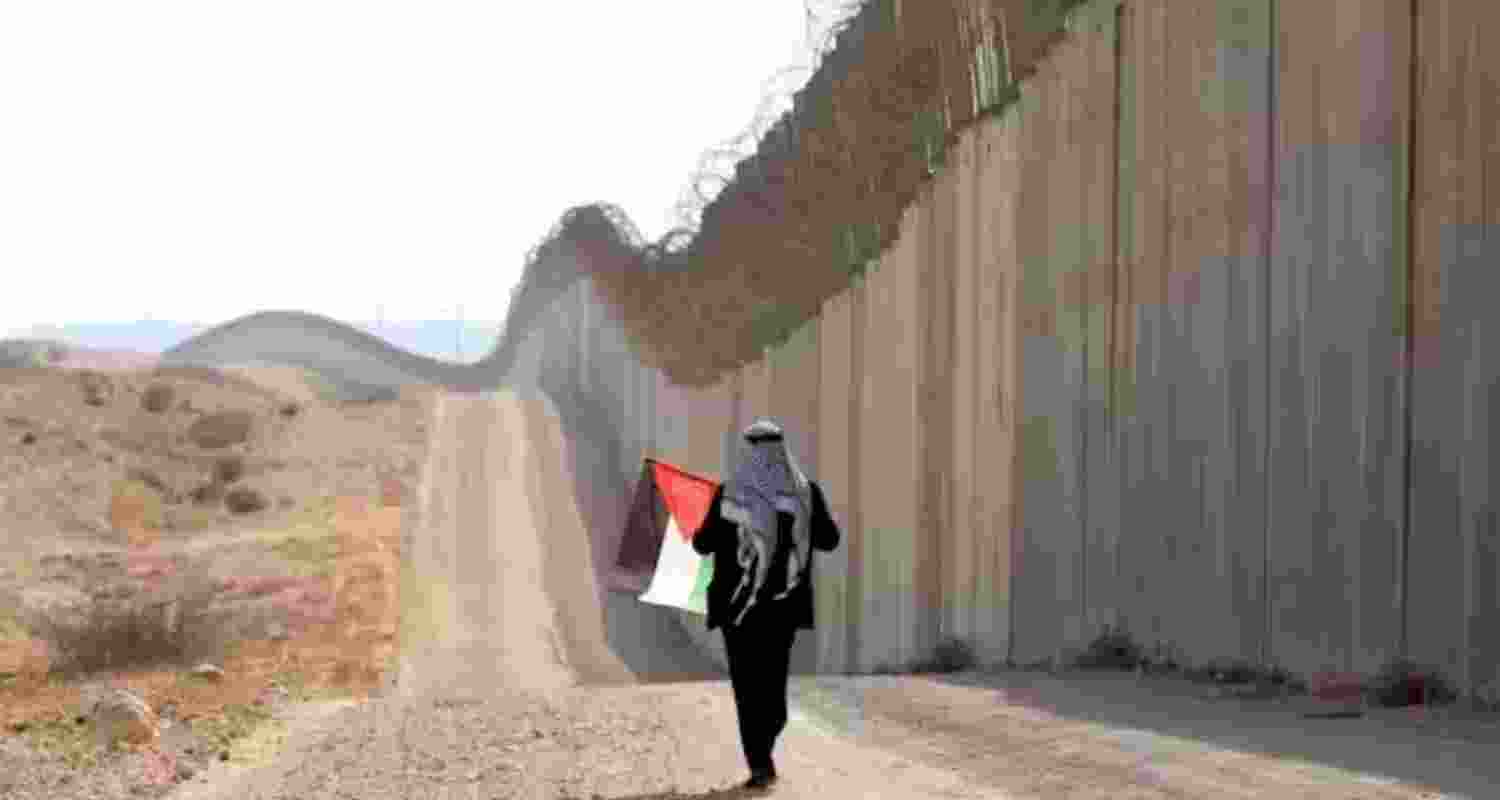 A man walks with a Palestinian flag in front of the Israeli separation barrier near Hebron in the West Bank in 2022. A man walks with a Palestinian flag in front of the Israeli separation barrier near Hebron in the West Bank in 2022.