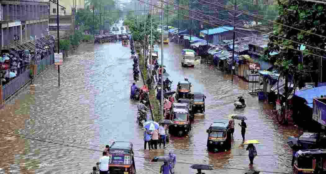 Commuters make way through a waterlogged road amid rainfall, in Palghar, Maharashtra. Commuters make way through a waterlogged road amid rainfall, in Palghar, Maharashtra.